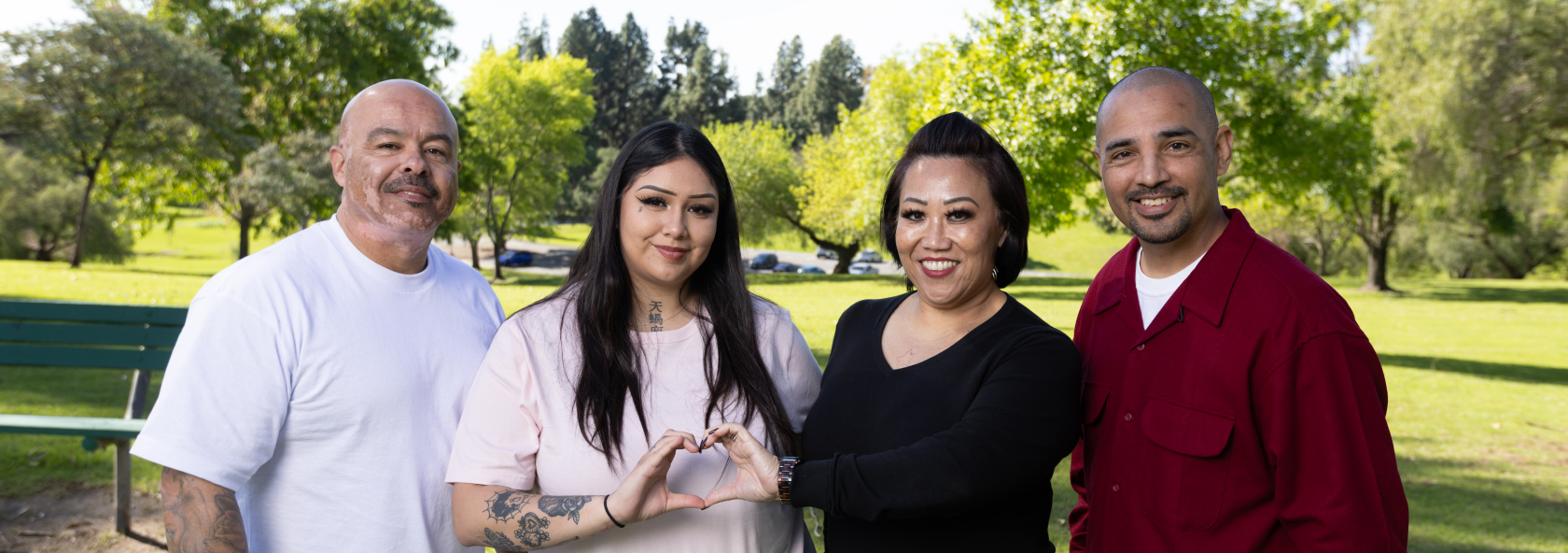 Four people standing together in a park, smiling and forming a heart shape with their hands to symbolize support, connection, and community.