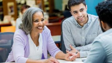 Confident African American senior businesswoman discusses something with colleagues during weekly meeting.