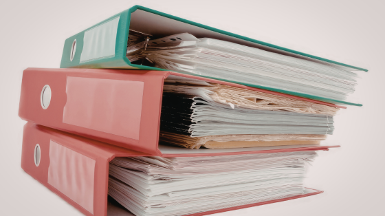 A stack of three binders, one teal and two coral, filled with papers and documents.