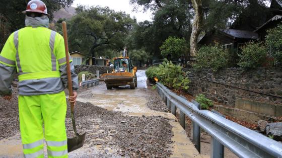 OC Public Works worker stands amid debris flow with a loader in the background.