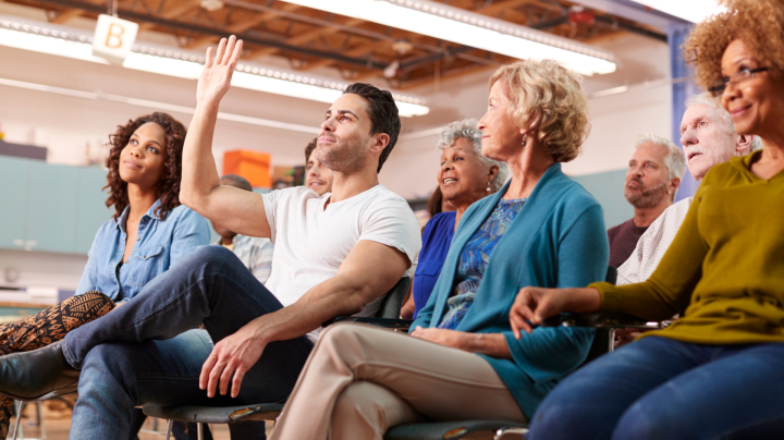a group of people sitting in a classroom and raising their hands