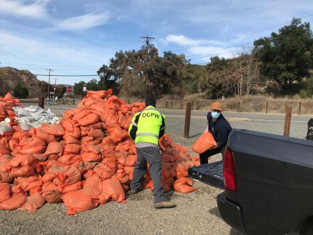 Workers load sand bags from a giant pile into the back of a pickup truck.